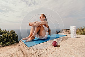 Woman sea pilates. Sporty happy middle-aged woman practices pilates on a beach near the sea, promoting a healthy