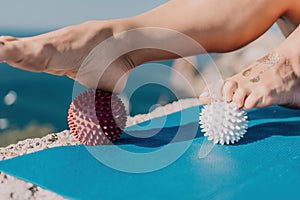 Woman sea pilates. Sporty happy middle aged woman practices pilates on yoga mat by the sea, using massage balls and