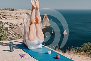 Woman sea pilates. Sporty happy middle aged woman practicing fitness on yoga mat with balls and roller near sea, smiling