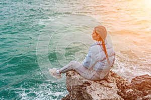 woman sea travel. A woman in a blue jacket sits on a rock above a cliff above the sea, looking at the stormy ocean. Girl