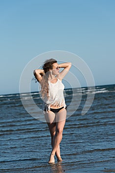 Woman in sea water wear bikini, sunglasses and white shirt