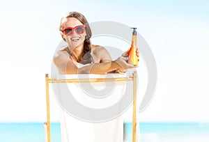 Woman on seacoast showing sun block while sitting in chair
