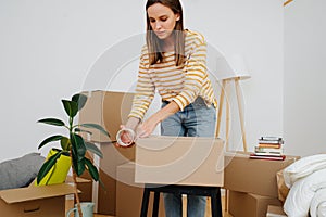 Woman sealing cardboard box, she`s moving out from old apartment to a new one