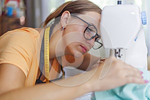 Woman seamstress in glasses works on sewing-machine at her workplace in workshop