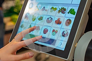 A woman is searching an appropriated fruit product on the screen of electronic balances for weighing