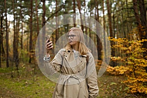 Woman searching for the mobile coverage on the mobile phone stands in a autumn forest, no service screen