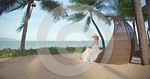 Woman seats on the beach loge against the ocean, camera moves to her