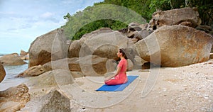 woman seats in meditation pose, she is on the beach by the sea line against tropical forest
