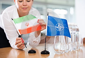 Woman secretary prepares an office for negotiations - she places flags of NATO (OTAN) and Iran table