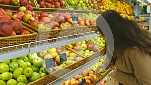 Woman selecting fresh red apples in grocery store produce department and putting it in plastic bag. Young pretty girl is