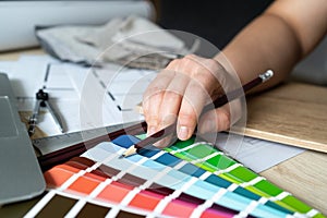 Woman selects paint from color scheme palette guide catalog with swatches at design studio desk.