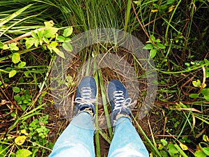 Woman selfie feet wearing dirty sneakers and blue jeans on green wild grass