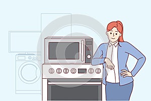Woman selling household appliances stands near oven and washing machine and looks at camera