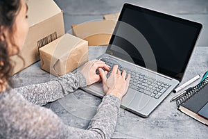 Woman sending parcel using her laptop. Working from home