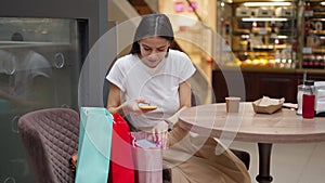 woman sending photo of her purchases from smartphone to friend while sitting in cafe after shopping