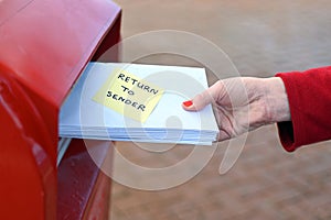 Woman sending return to sander letters in envelope in red mail box