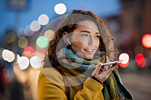 Woman sending voice note on city street in winter night