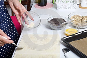 A woman sends puff pastry with sugar. For making puff pastry curls with poppy and walnut filling. Nearby on the table are