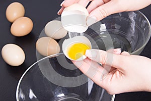 Woman separate egs in glass bowl on black table photo