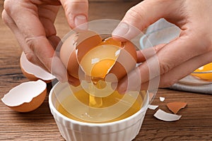 Woman separating egg yolk from white over bowl at wooden table, closeup