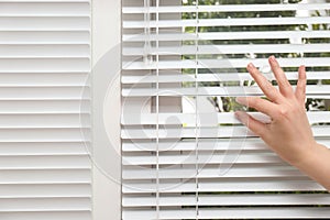 Woman separating slats of window blinds