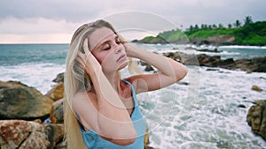 Woman in serene contemplation amid rocky coast. Gentle waves back sunlit, peaceful, self-care moment. Blonde, sea breeze