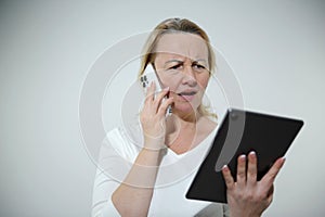 woman Seriously tense and annoyed talking on phone looking at tablet she does not like rise in prices unhappy with