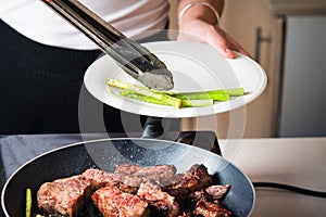 Woman serving beef steak with baby asparagus on the pan