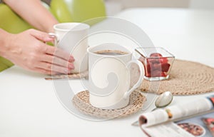 woman serving a coffee in a white light kitchen using eco knit jute tablemats. good morning concept. crop view.