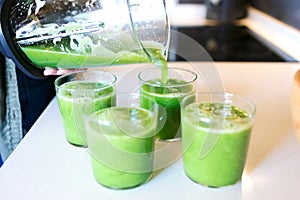 Woman serving detox green juice into glasses at home.