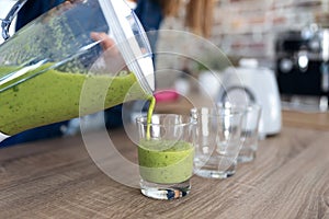 Woman serving detox green juice into glasses at home