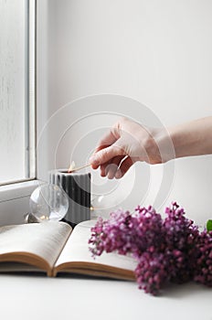 Woman sets fire to a candle. Beautiful composition with opened book and flowers