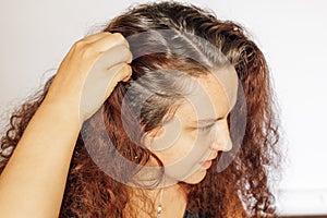 Woman setting back right side of hair to show graying roots on white background. Regrown roots which are in need of