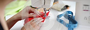 Woman sew on red fabric on a sewing machine