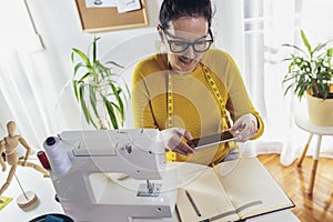 Woman sewing on a sewing machine at her home using phone