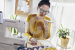 Woman sewing on a sewing machine at her home using phone