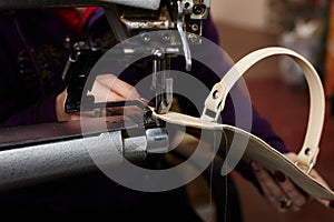 A woman sews a leather strip with a special sewing machine for leather, used in the production of handbags /shoes