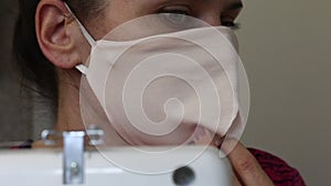 A woman sews a protective mask from fabric. Trying it on himself. Near the sewing machine. Work at home