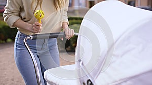 Woman shaking rattle toy front of newborn in stroller, babyhood interaction