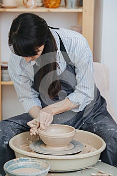 Woman shaping clay bowl on a pottery wheel in her private workshop