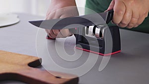 A woman sharpens a kitchen knife in a knife sharpener on the table