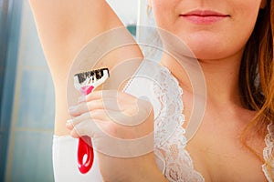 Woman shaving armpit with razor in bathroom