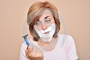 Woman with shaving foam on her face holding and looking sadly at a razor