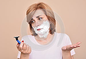 Woman with shaving foam on her face holding and looking sadly at a razor