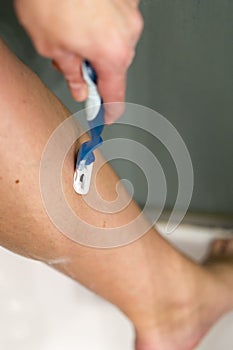 Woman shaving her legs. Woman in the shower shaves. Sexy young woman shaving her leg in shower cabin. Close-up view of female leg