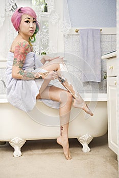 Woman shaving her legs on the side of the bathtub