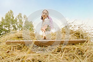 A woman in a shawl turns hay with a wooden rake. Haymaking season