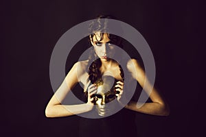 Woman with shining makeup and braids holding golden mask