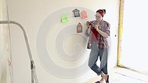 A woman in shirt and jeans is watching a video tutorial on renovating a room.