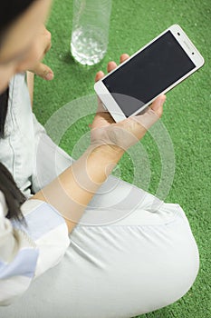 Woman in shirt playing on phone, sitting on a green floor with legs crossed